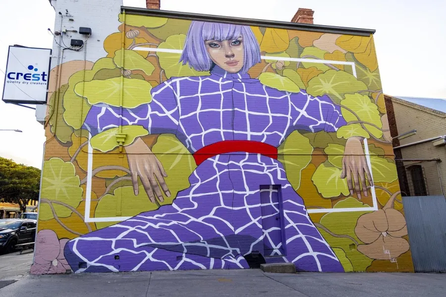 Eden Large scale mural of a woman in a purple jumpsuit on a yellow background painted on the side of a building