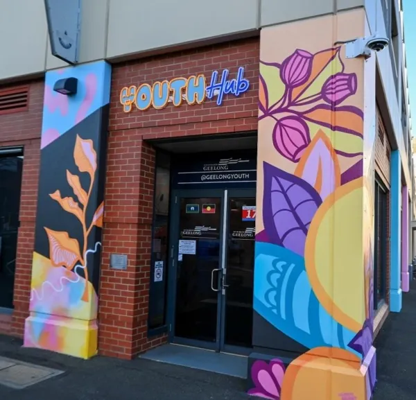 The Nest Youth Hub - Main Entry Artwork by Leah Grant Entrance to the Geelong Youth Hub, with a brick doorway framed by colourful mural-painted columns featuring abstract leaves and shapes in purple, yellow, blue and orange.