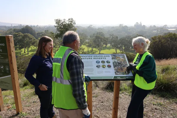 Environment and Biodiversity officer Kate Constance with Geelong Field Naturalist Club member Rod Lowther and Cr Elise Wilkinson at Seaview Grassland Nature Reserve. Environment and Biodiversity officer Kate Constance stands with Geelong Field Naturalist Club member Rod Lowther and Cr Elise Wilkinson around a Seaview Grassland Nature Reserve information sign.