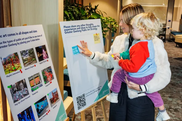 Community consultation for the Greater Geelong Public Art Strategy. A community member is holding a small child while providing feedback at a community consultation for the Greater Geelong Public Art Strategy.