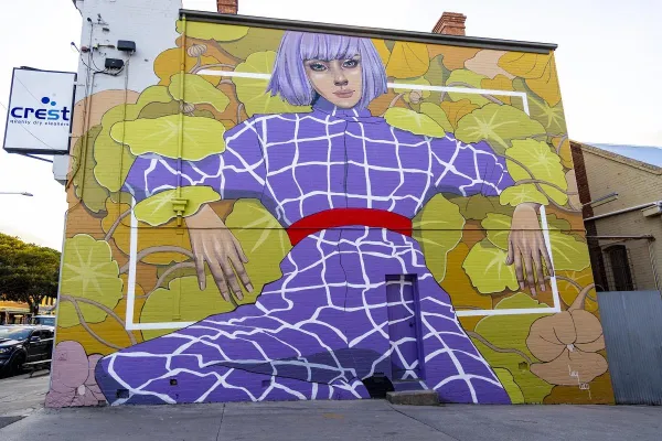 Eden Large scale mural of a woman in a purple jumpsuit on a yellow background painted on the side of a building