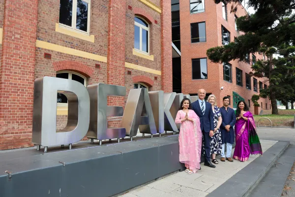 Mayor Kontelj OAM and Deakin Acting Vice-Chancellor Professor Susan Elliott AM with Deakin alumni Ashwini (also performing at event), Deakin staffer Mohan and Deakin staffer Ambili Five people standing in front of Deakin signage, some are wearing traditional cultural dress.